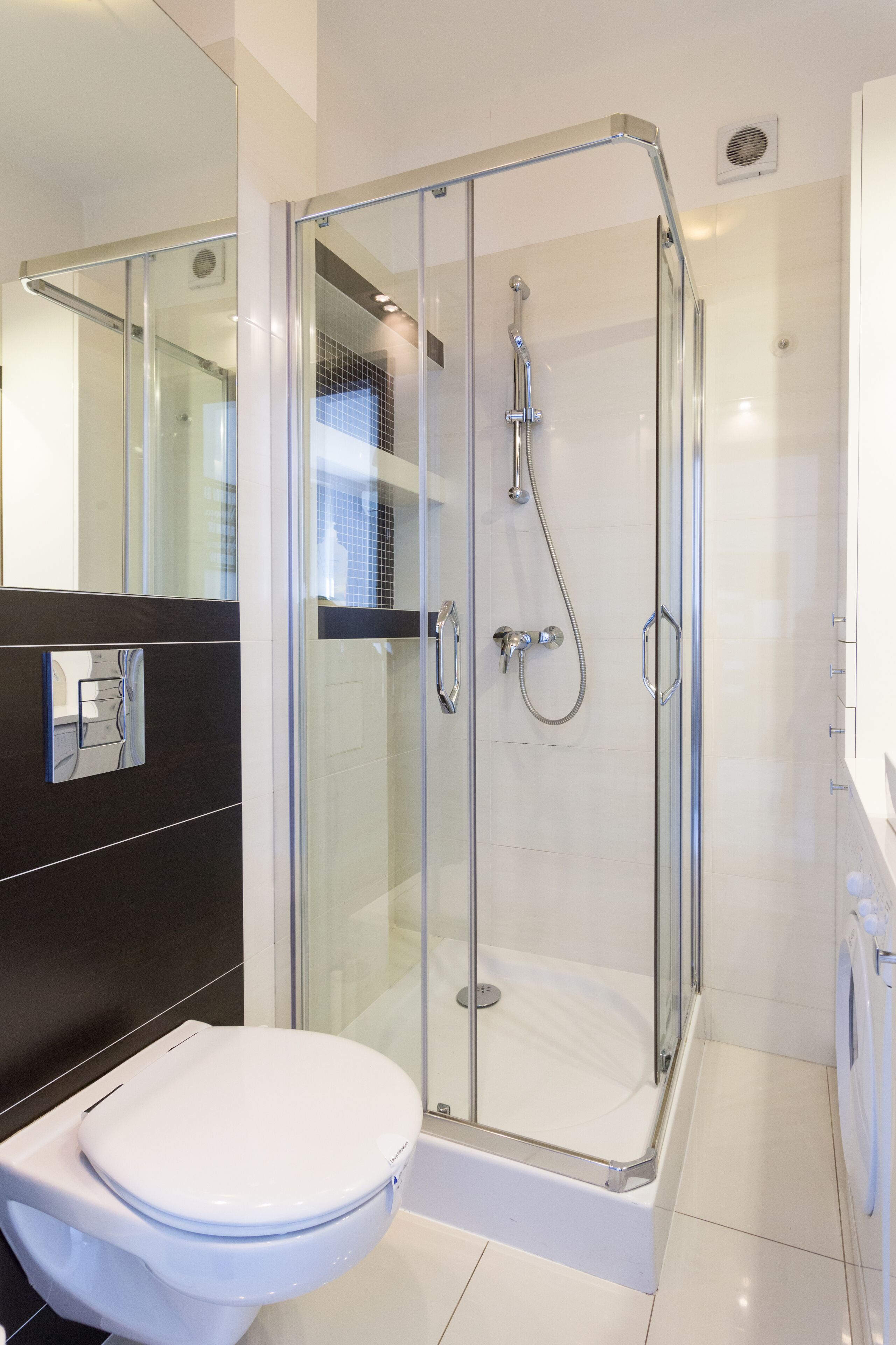 Un baño moderno con ducha de vidrio, inodoro blanco y pared de azulejos negros.