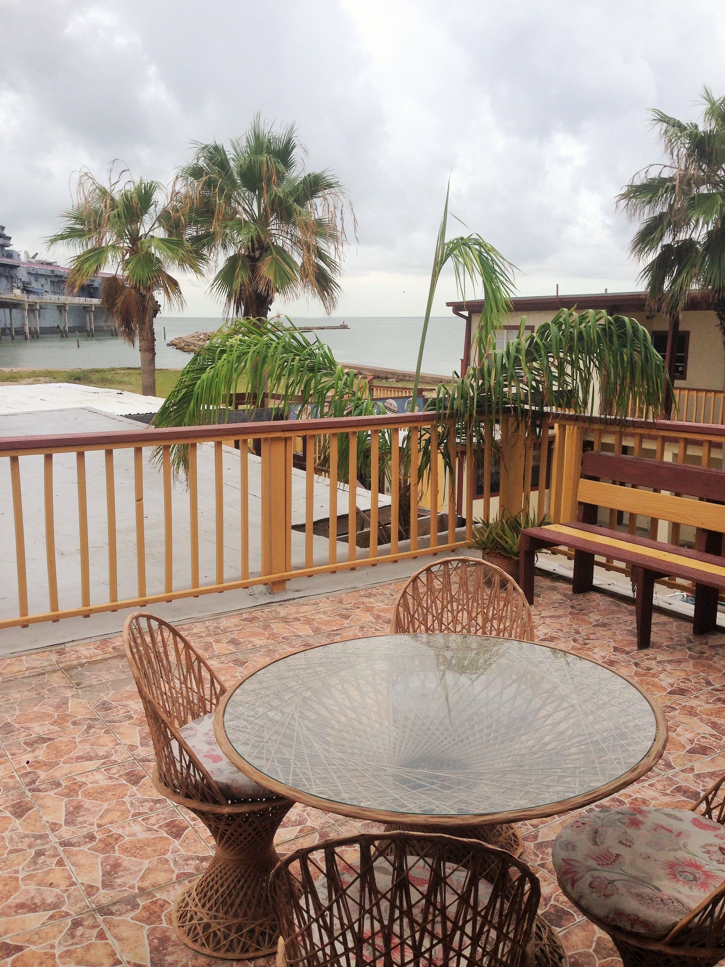 A patio with wicker furniture, a glass table, and a view of the sea.