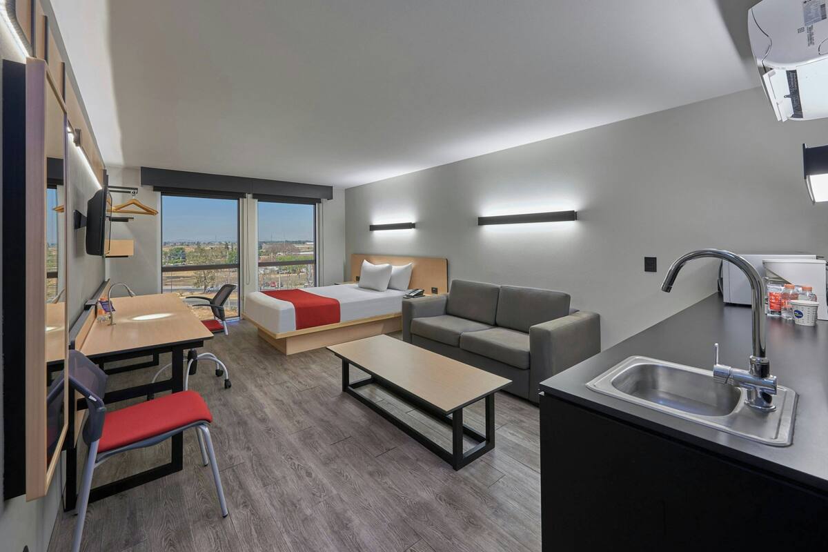 Una habitación de hotel moderna con cama, sofá, mesa de comedor y kitchenette.