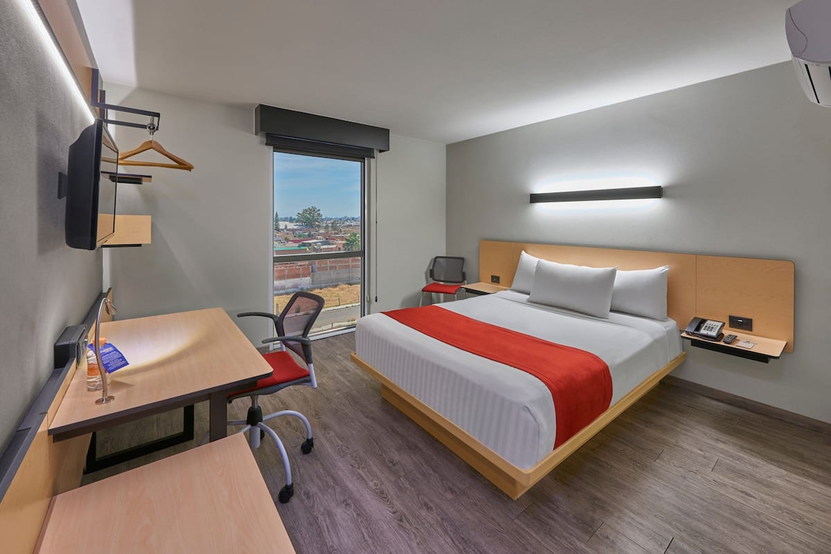 Habitación de hotel con cama, escritorio, silla y vistas a la ciudad.