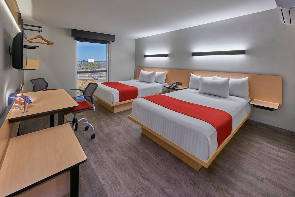 Habitación de hotel con dos camas, un escritorio, sillas y un televisor.