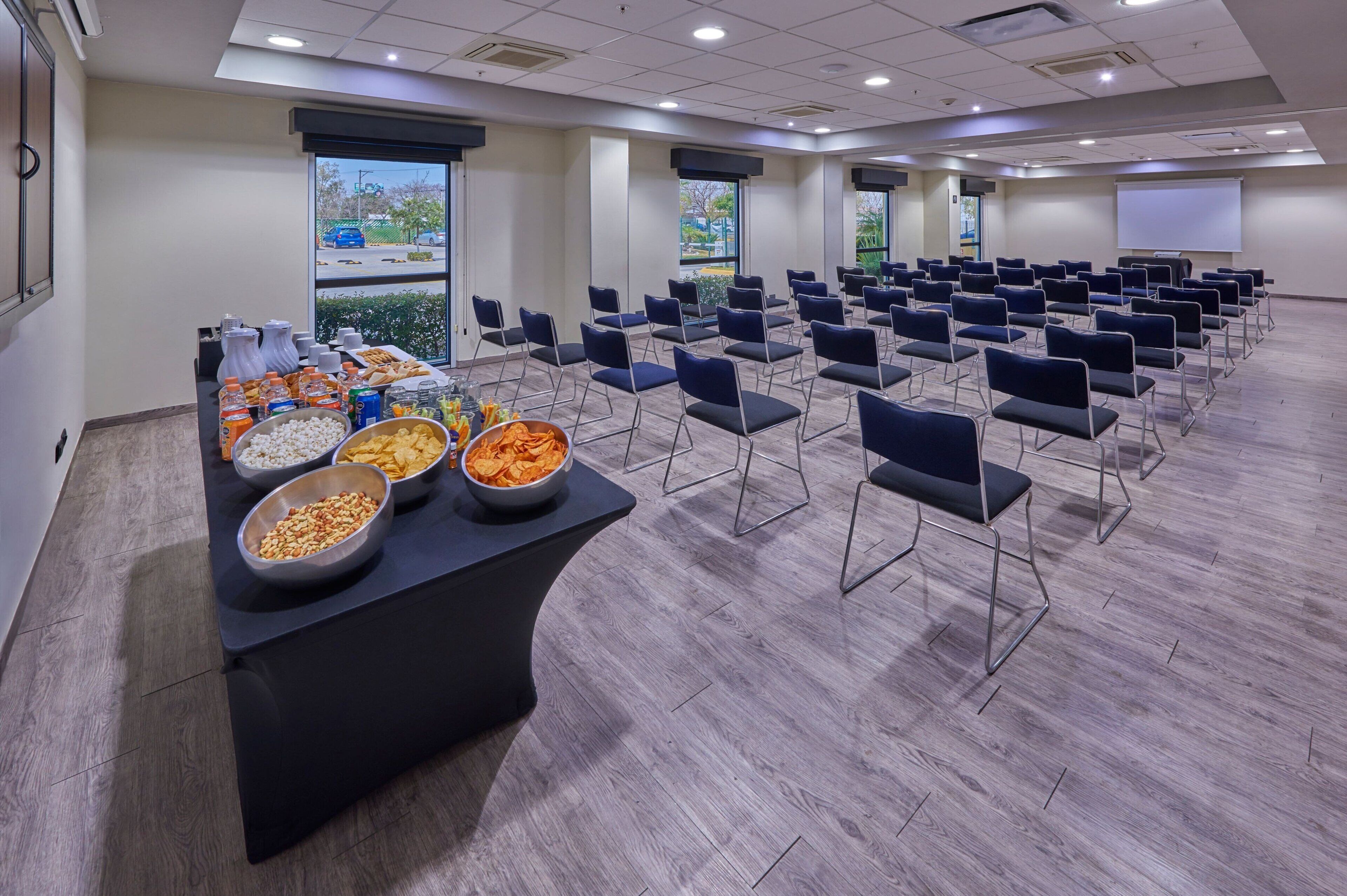 A conference room with rows of chairs, a buffet table with snacks, and a projector screen.