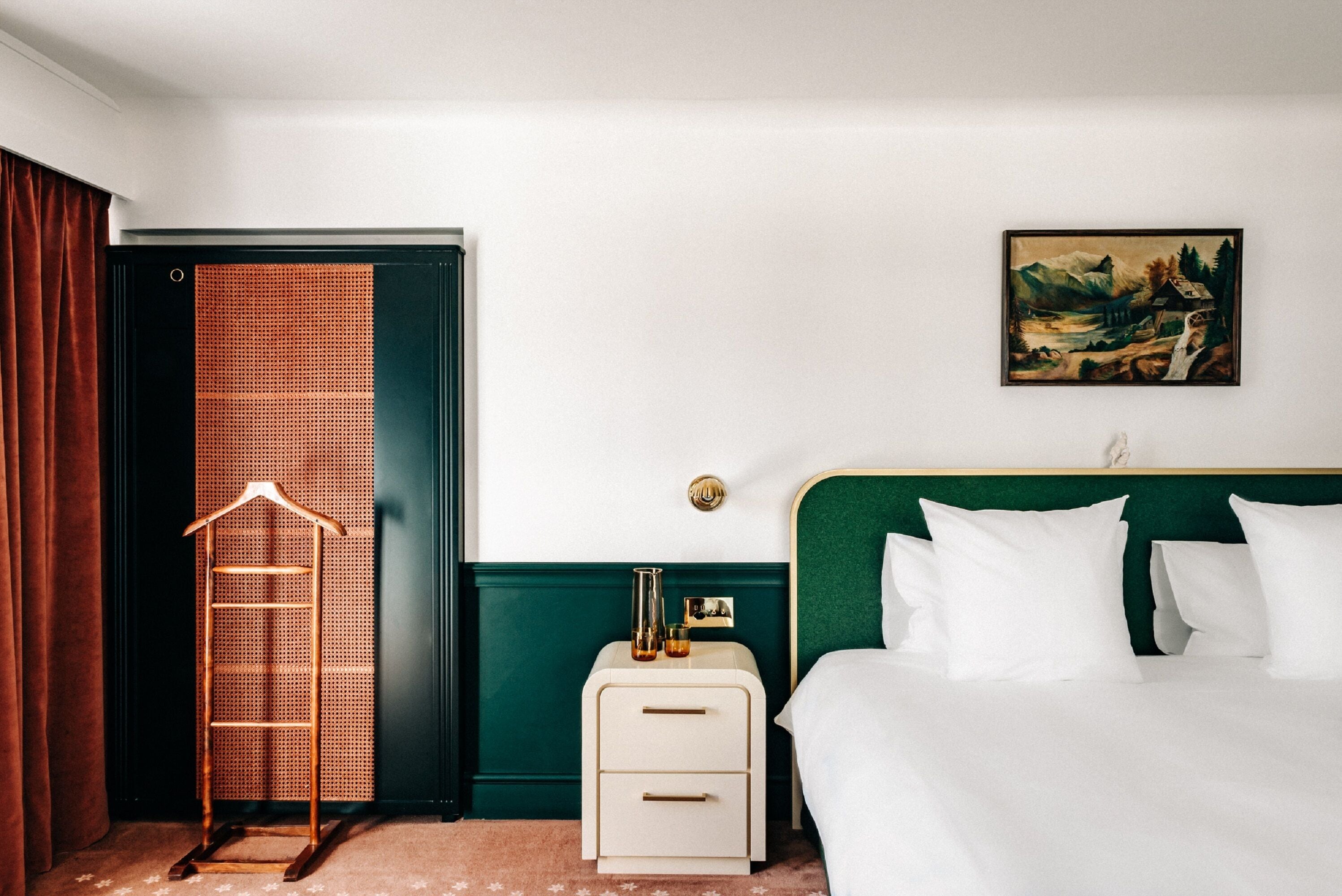 Ein Hotelzimmer mit Bett, Nachttisch, einem an der Wand hängenden Gemälde und einem hölzernen Kleiderbügel.