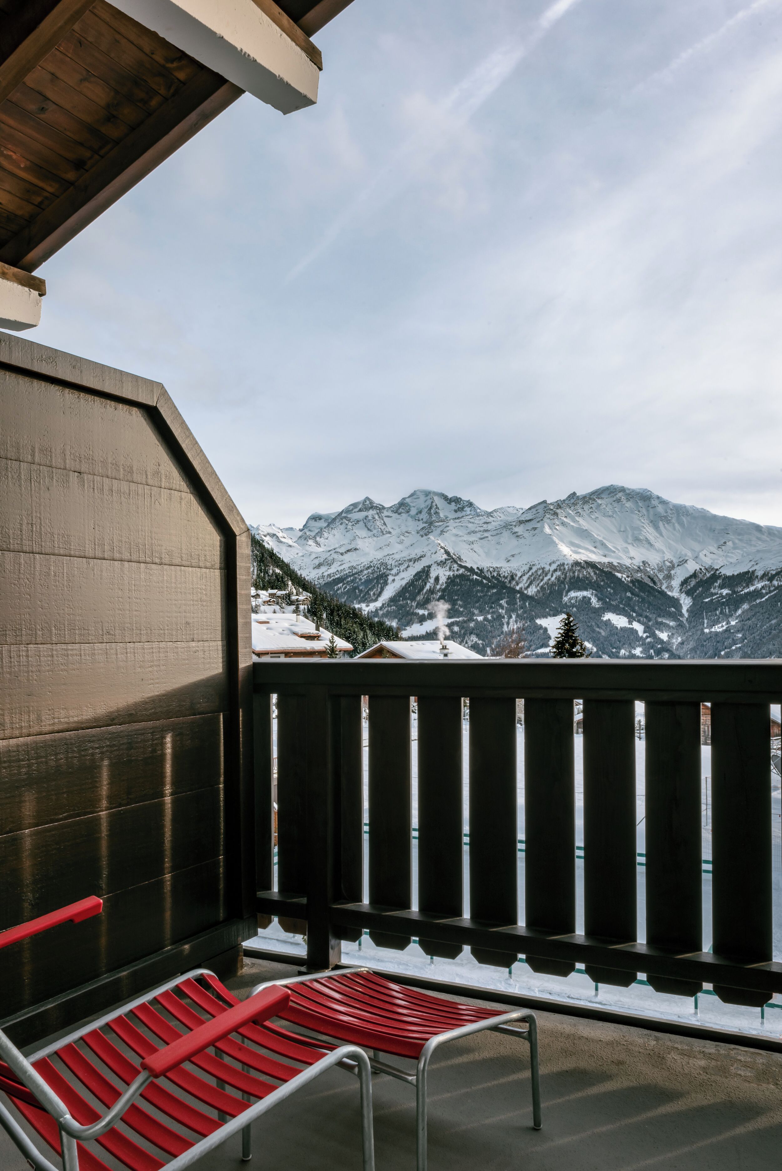 A balcony with red metal chairs and a view of snow-covered mountains.