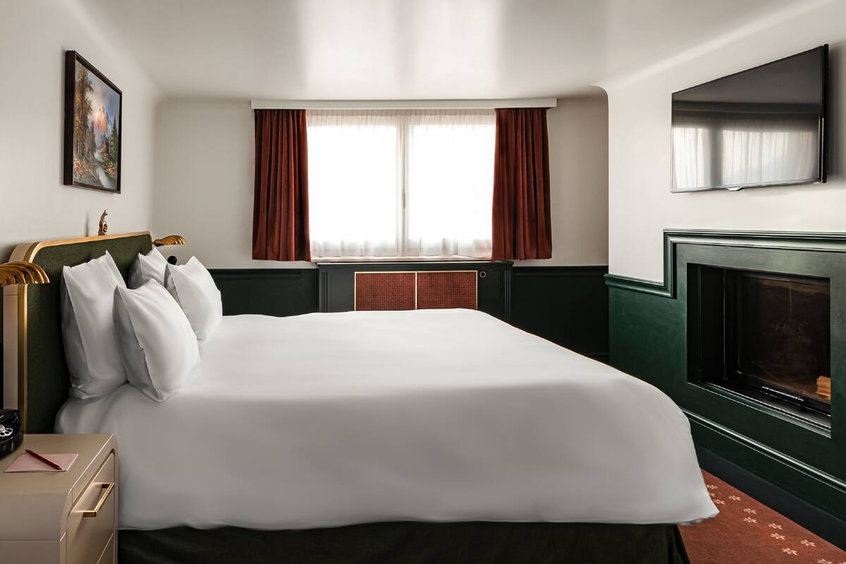 A hotel room with a large bed, a television, a fireplace, and a window with curtains.