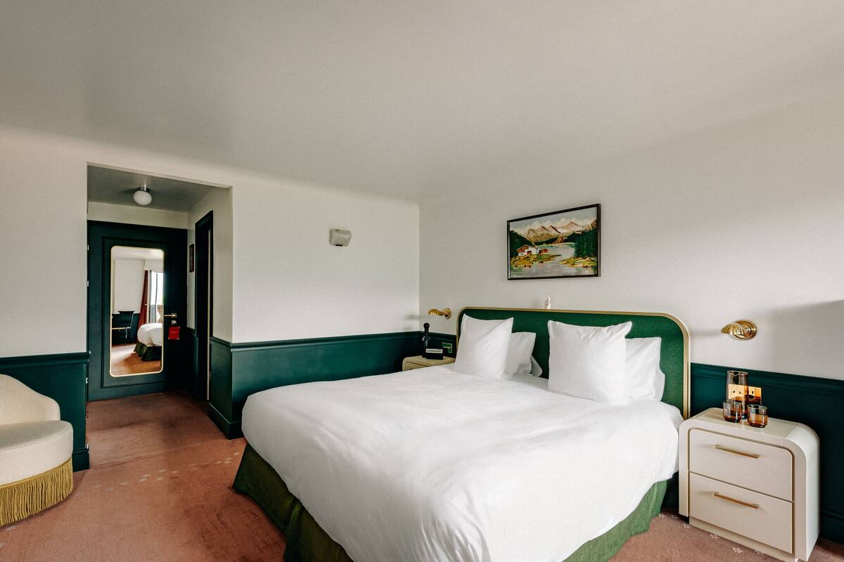 A hotel room with a large bed, a nightstand, a chair, and a painting on the wall.