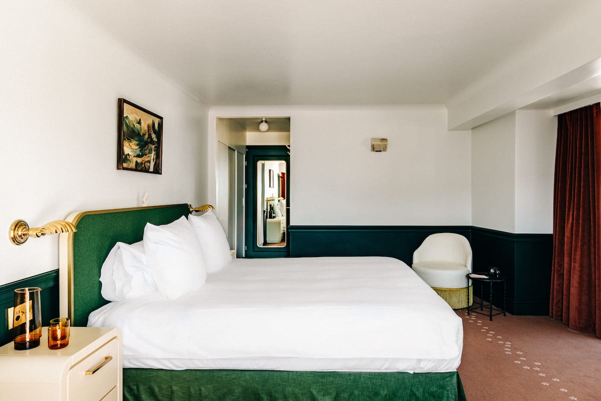 A hotel room with a large bed, a bedside table, a chair, and a mirror.