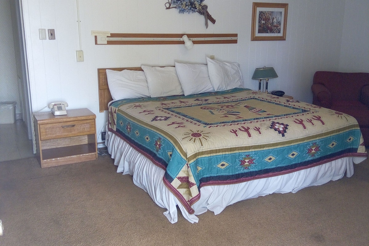 A bedroom with a bed, a nightstand, a lamp, a ceiling fan, and a wall decoration.