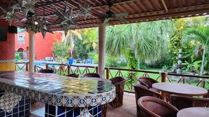 An outdoor patio with a tiled bar area, wicker chairs, and a view of a lush garden.