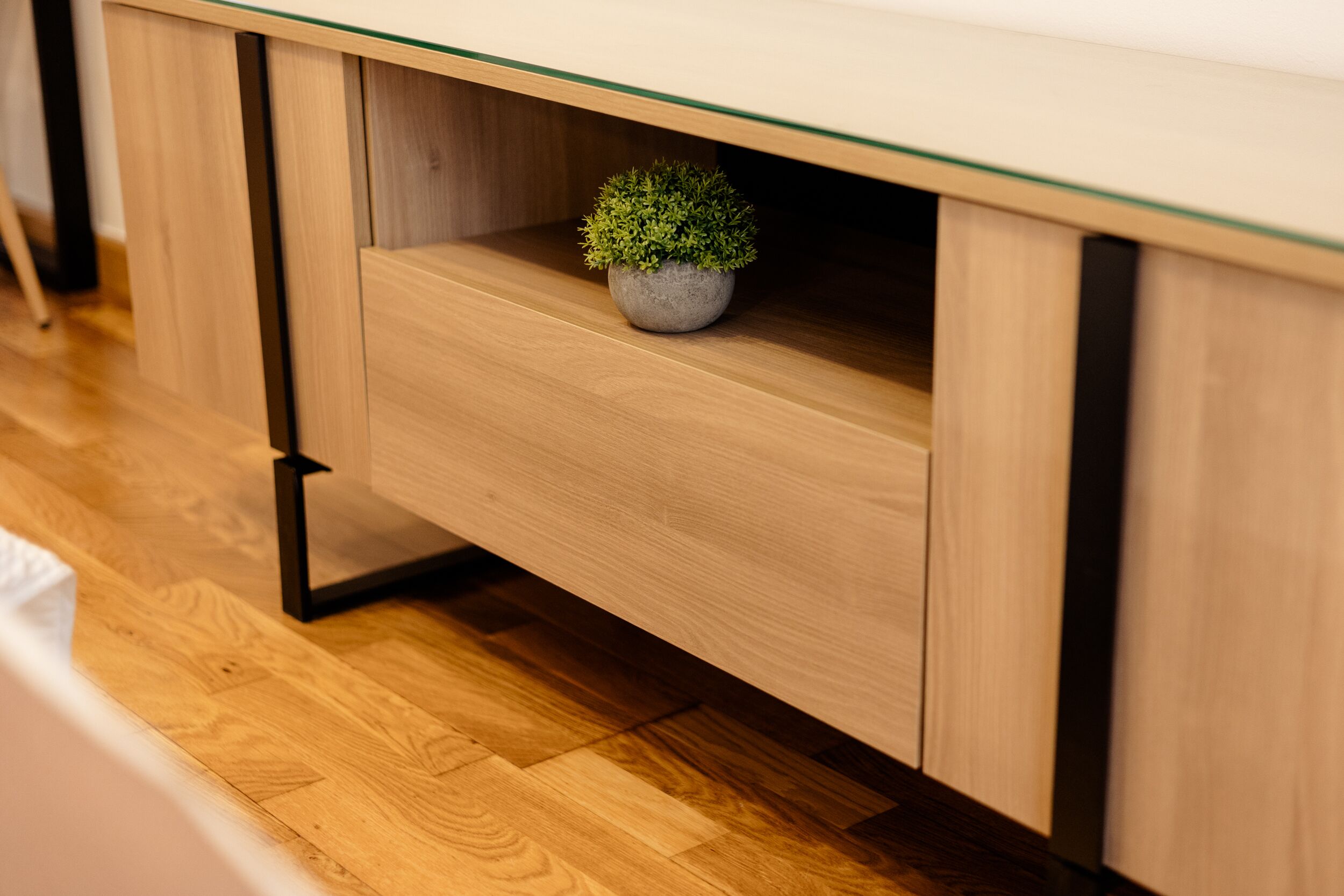 Un bureau en bois avec un plateau en verre et une petite plante en pot posée dessus.