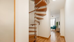 A modern interior with a wooden spiral staircase, a wooden floor, and a view into a living area with a sofa and a plant. - Debambú (Málaga)