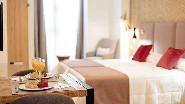 A hotel room with a neatly made bed, a dining table with breakfast, and a view of the room's interior. - Debambú (Málaga)