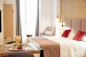 A hotel room with a neatly made bed, a dining table with breakfast, and a view of the room's interior. - Debambú (Málaga)