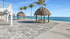 A beachside walkway with thatched umbrellas, palm trees, and a view of the sea. - 1 Island Hideaway in the Keys (Marathon)