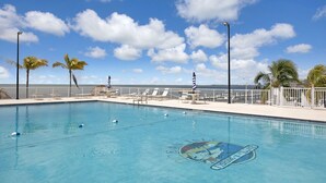 A swimming pool with lounge chairs and umbrellas, surrounded by a white fence, with a clear view of the ocean and a blue sky. - 1 Island Hideaway in the Keys (Marathon)