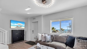A modern living room with a sectional sofa, a flat-screen TV, a black cabinet, and a large window with a beach view. - 1 Island Hideaway in the Keys (Marathon)