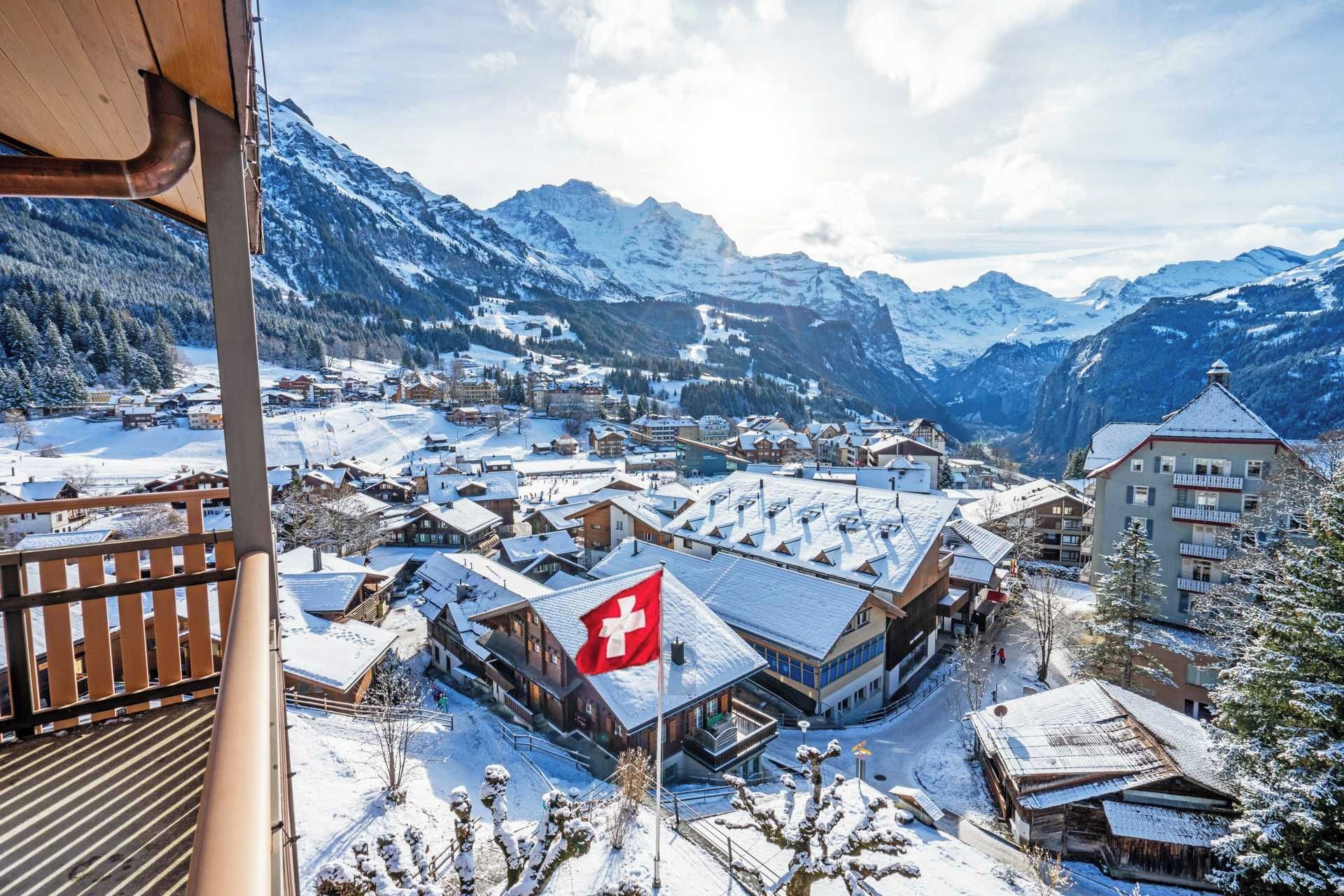 A snow-covered mountain town with traditional wooden buildings and a prominent Swiss flag.