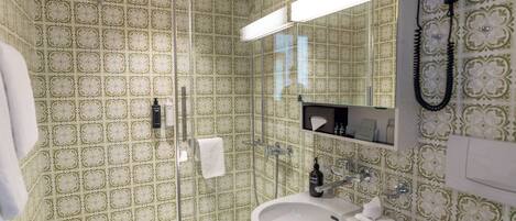 Un baño con papel tapiz estampado, cabina de ducha de vidrio, lavabo blanco y un espejo sobre el lavabo.