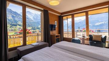 Ein Hotelzimmer mit Bett, Schreibtisch, Stuhl und einem Balkon mit Bergblick.