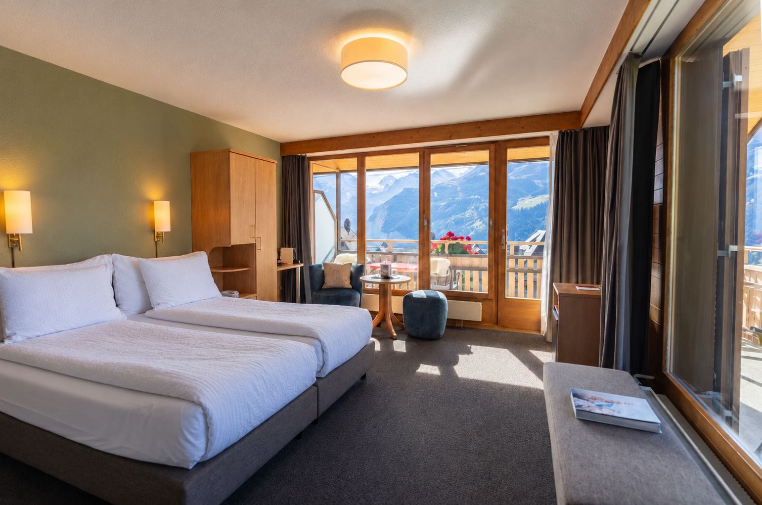 Une chambre d’hôtel dotée d’un grand lit, d’un coin salon avec une table et d’un balcon offrant une vue sur la montagne.