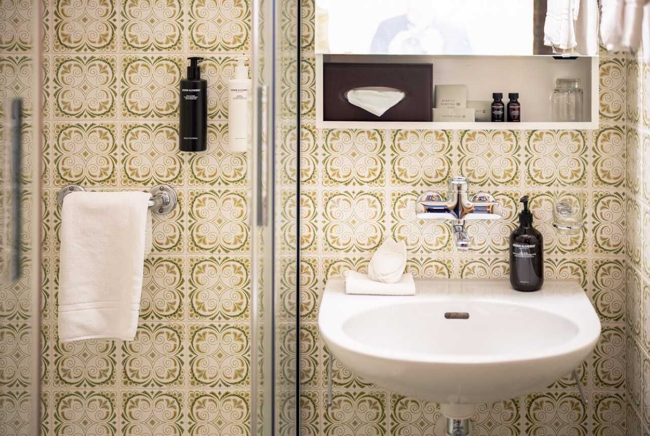 Een badkamer met behang met patroon, een witte wastafel en toiletartikelen aan de muur.