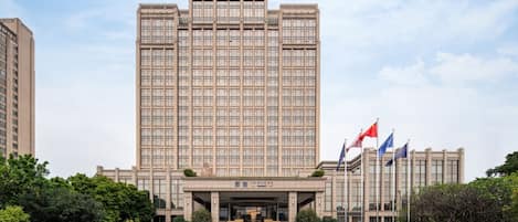 A large, multi-story building with a symmetrical facade, a central entrance, and multiple flags.