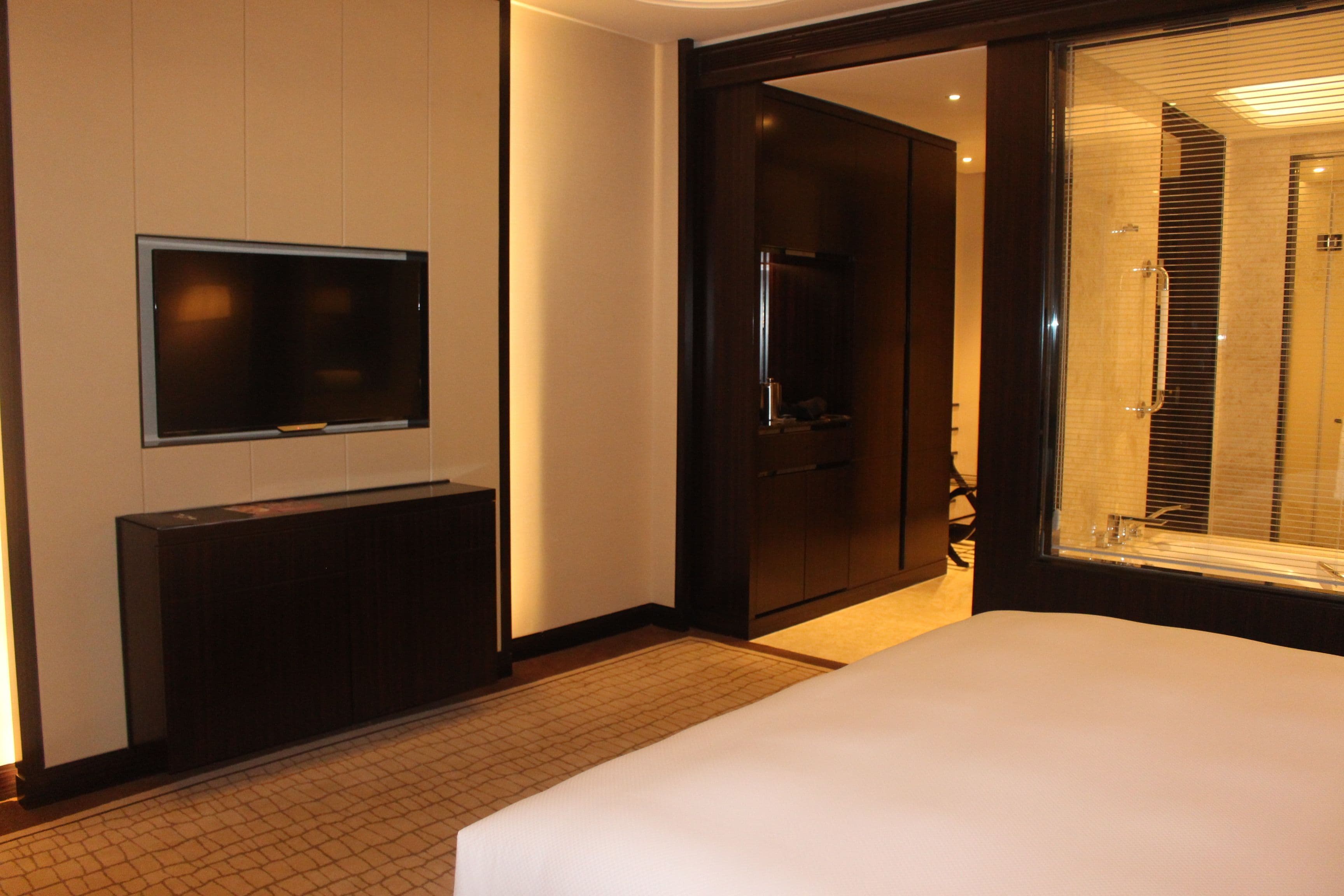 Une chambre d’hôtel comprenant un lit, un téléviseur fixé au mur, une porte donnant accès à une salle de bain et un sol carrelé.