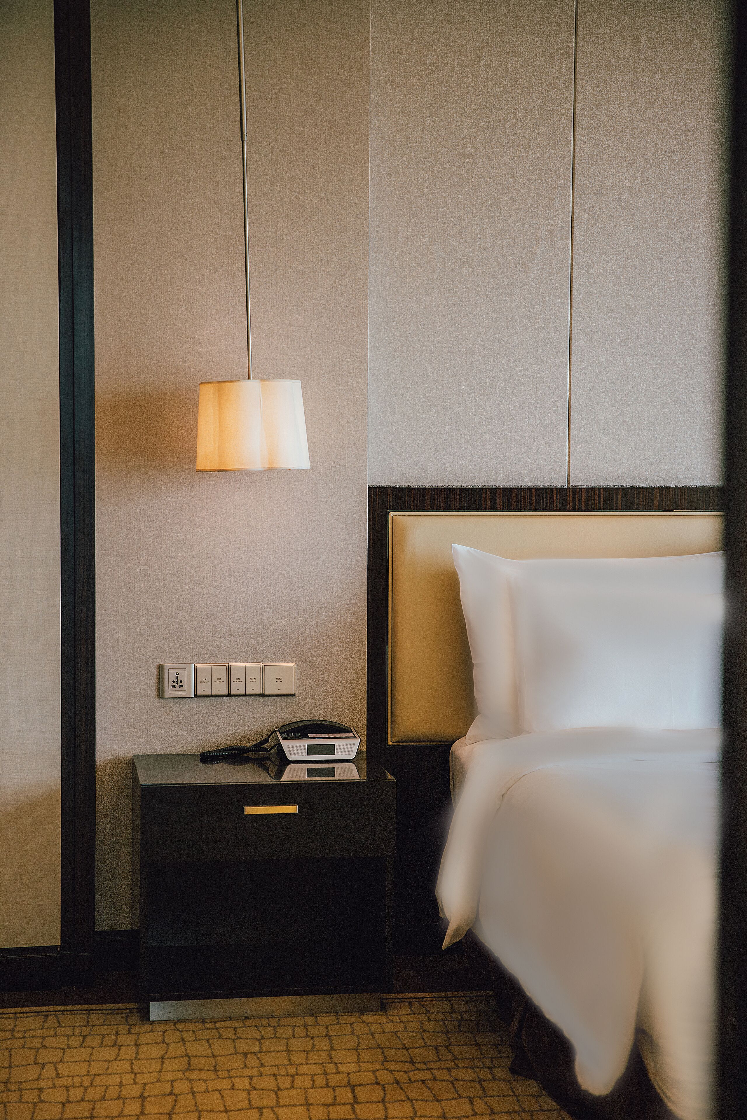 A hotel room with a bed, a nightstand, a lamp, and a power outlet.