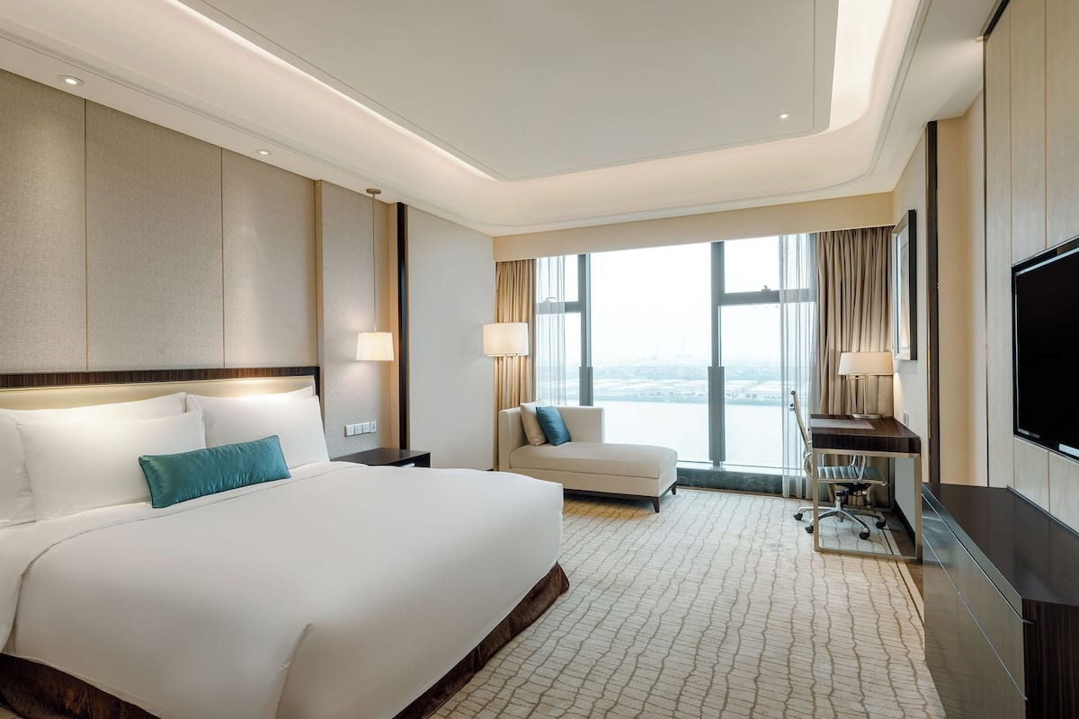 A modern hotel room with a large bed, a sofa, a desk, and a TV.