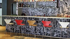 A bar area with a black and white mural, a variety of bottles, glasses, and a modern seating arrangement. - ibis Rio Branco (Rio Branco)
