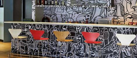 A bar area with a black and white mural, a variety of bottles, glasses, and a modern seating arrangement.