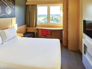A hotel room with a bed, a desk, a TV, and a window with a view of a cityscape.
