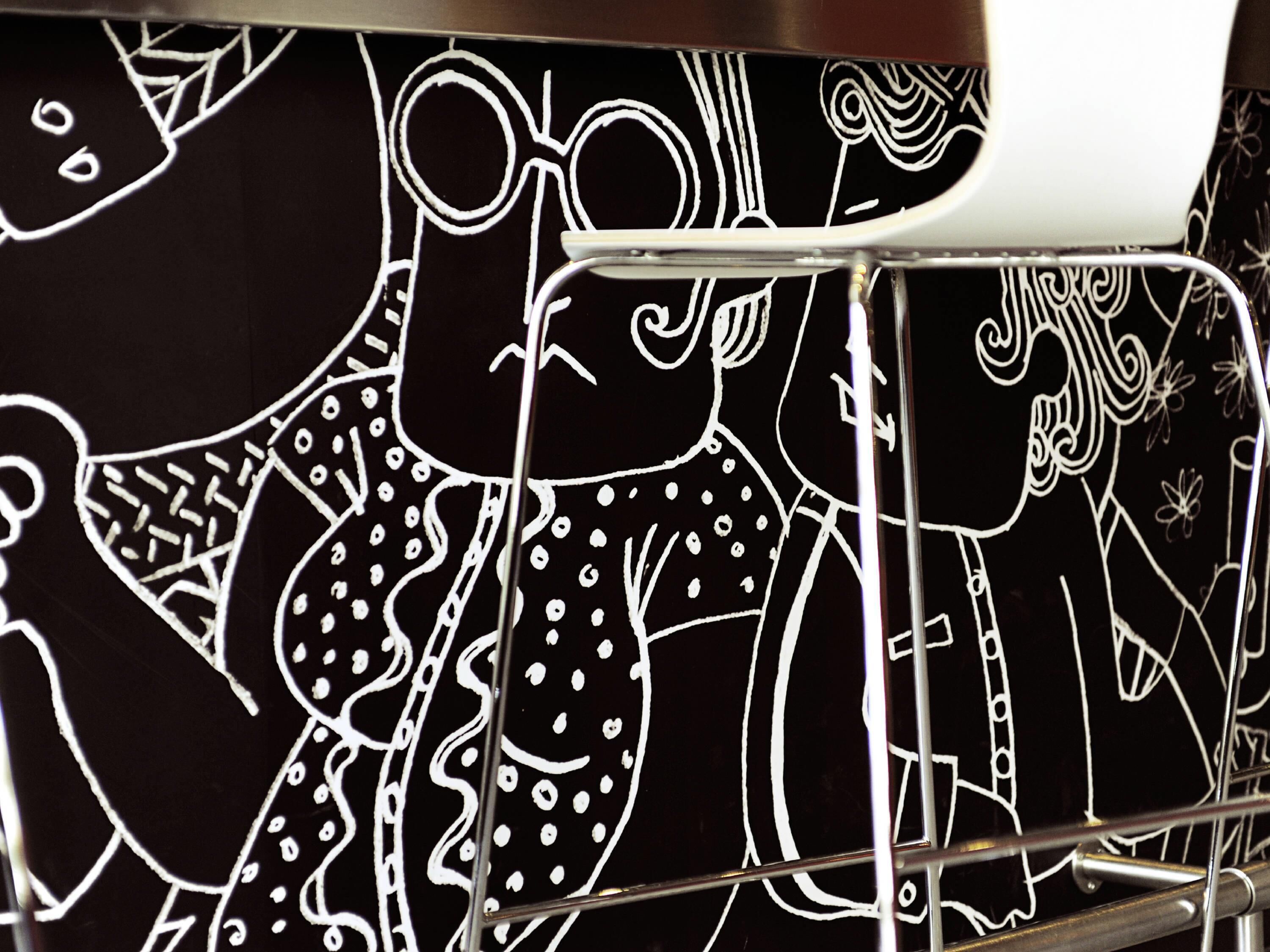 A close-up of a black and white line drawing on a surface, with a metal structure partially obscuring the view.