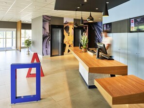 A modern reception desk with a computer, a potted plant, and a red and blue sign.
