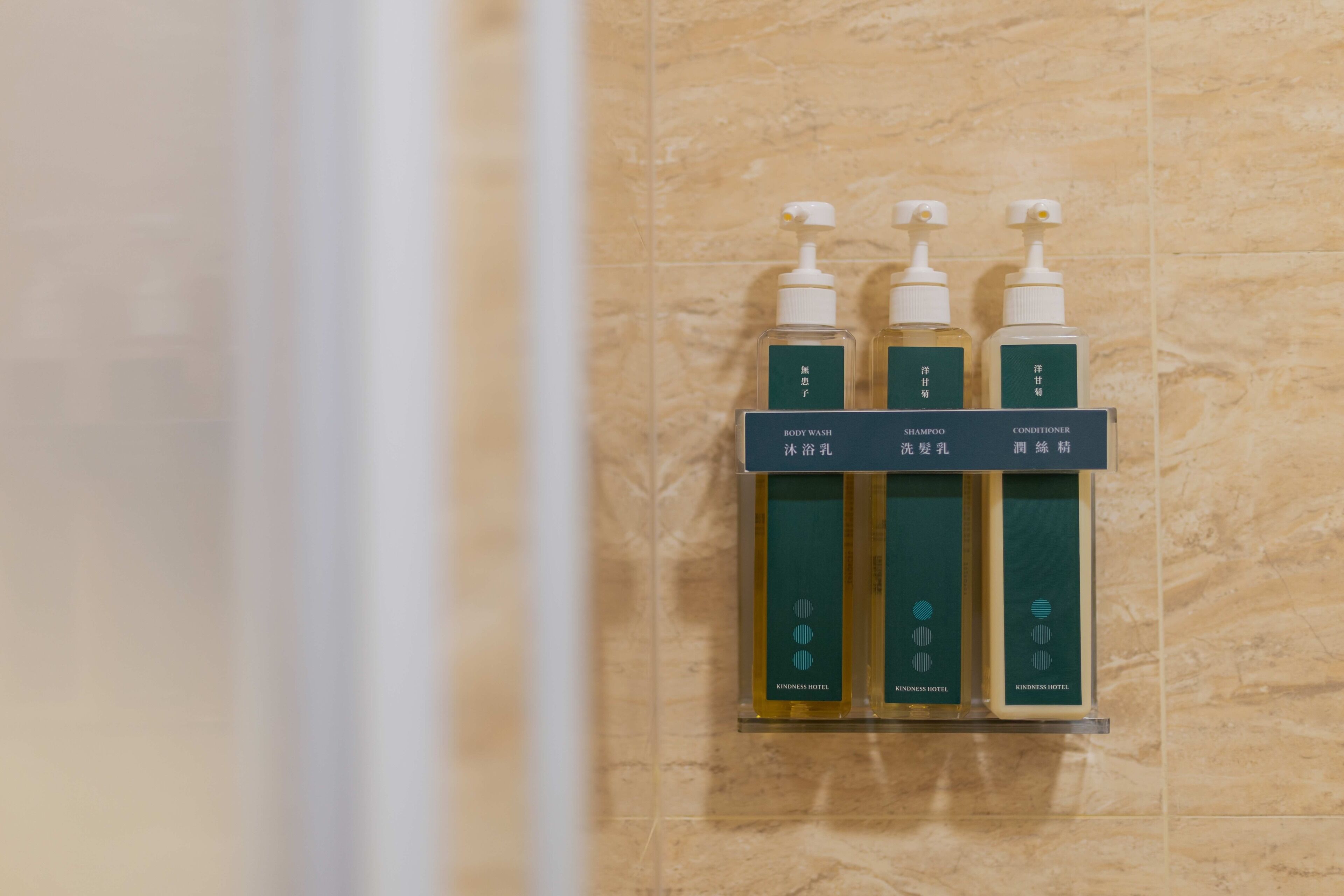 Un baño con pared de mármol y tres botellas de artículos de aseo en un estante.