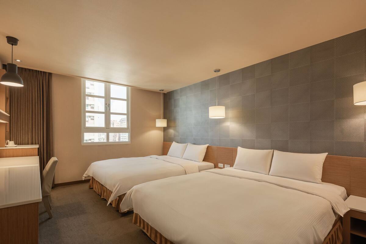 A hotel room with two beds, a desk, and a window.