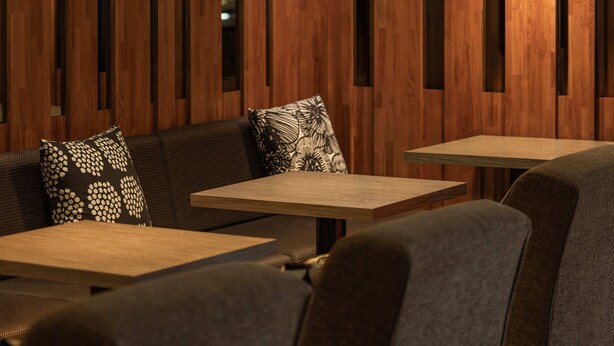 Un interior moderno con paneles de madera, tres lámparas colgantes y una zona de estar con cojines estampados.