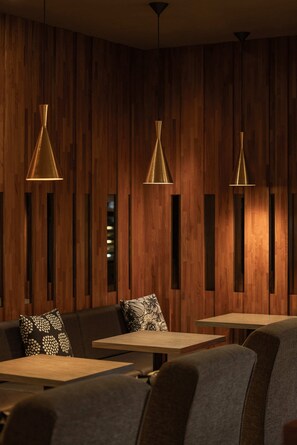 A modern interior with wooden panel walls, three pendant lights, and a seating area with patterned cushions.