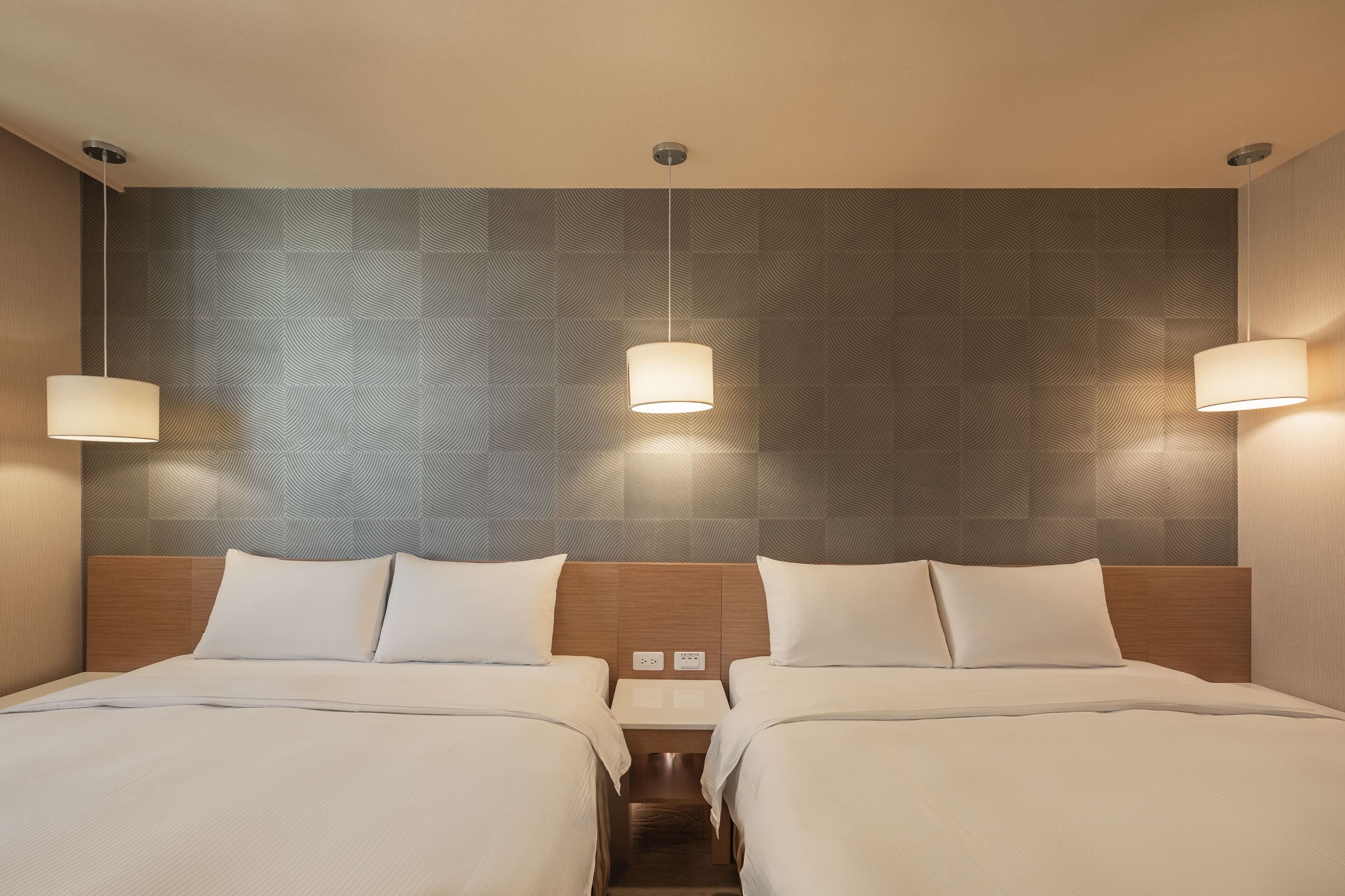 Quarto de hotel com duas camas, cabeceira de madeira e luminárias fixadas na parede.