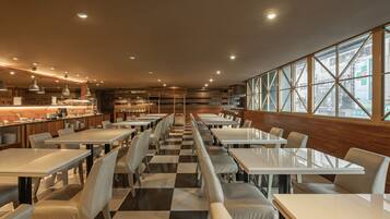 A spacious restaurant with high ceilings, modern lighting, and large windows offering a view of the city.