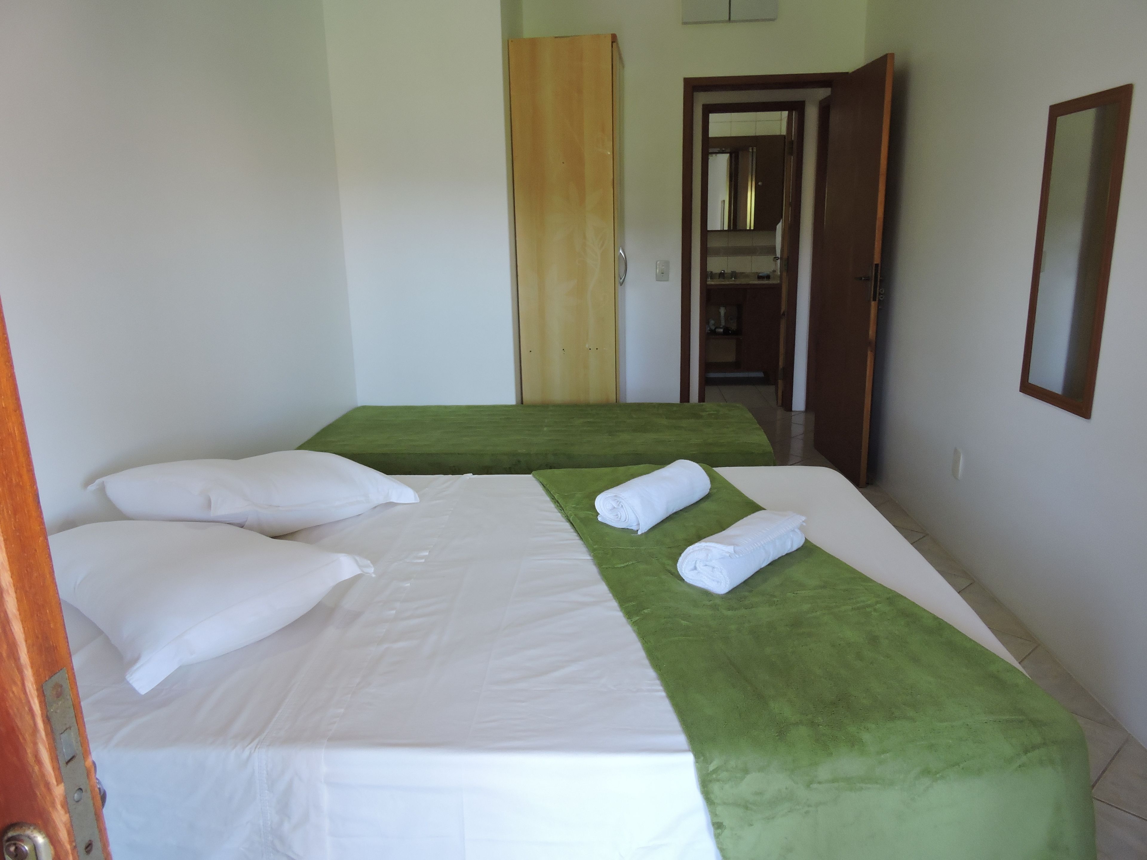 Habitación de hotel con dos camas, cada una con ropa blanca y cubrecamas verdes. Se ve un armario de madera y un espejo en la pared.