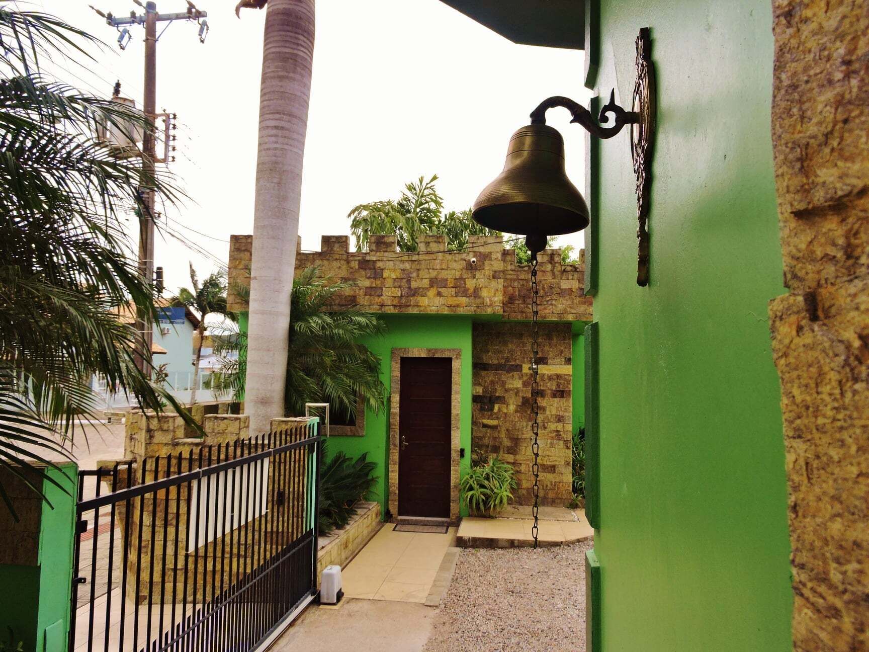 A green building with a stone wall, a metal gate, and a bell.