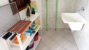 Un baño con lavamanos, espejo y estante con productos de limpieza.