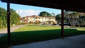 A covered outdoor area with a well-maintained lawn, several lounge chairs, and a building with multiple stories in the background.