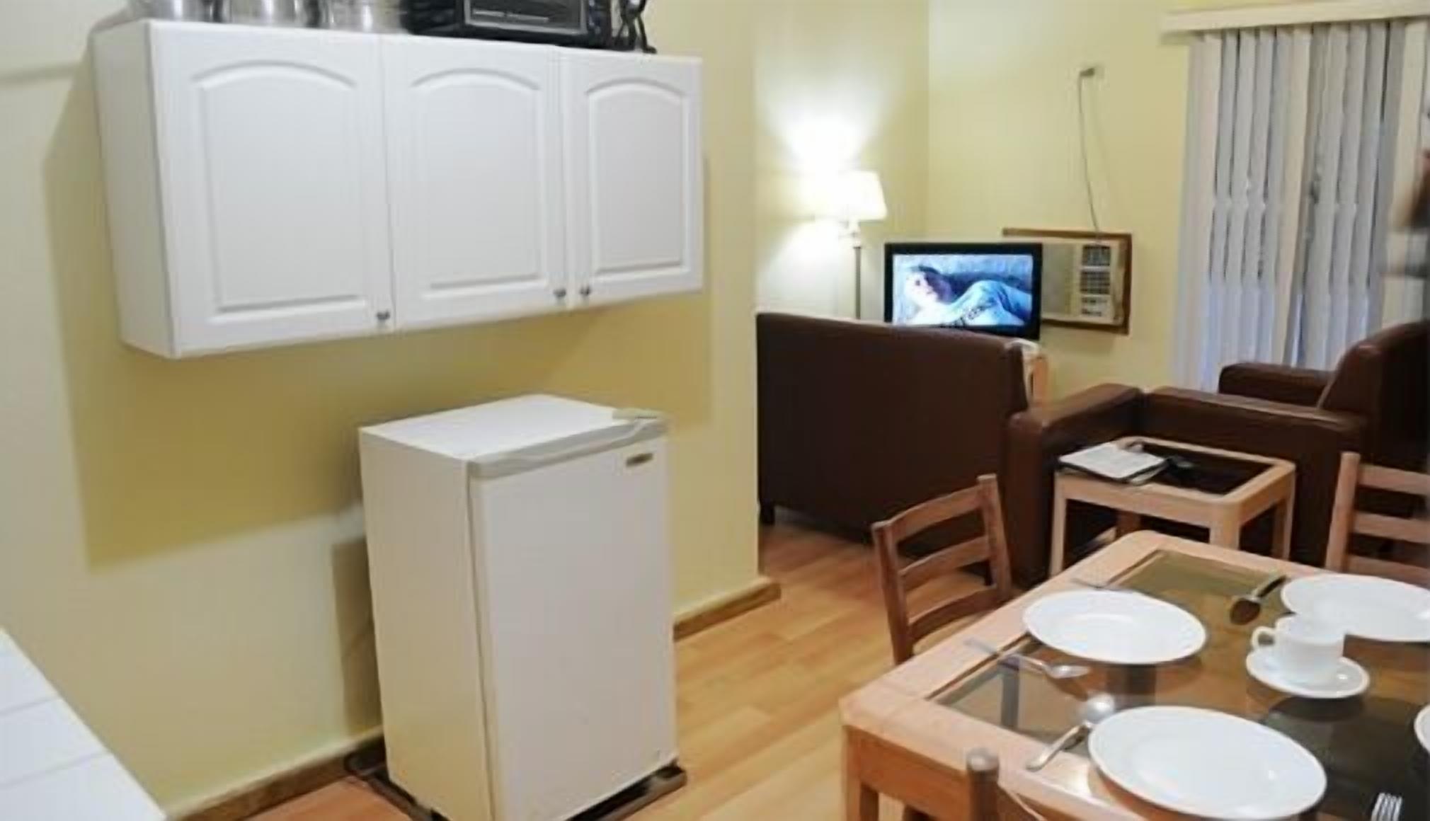 Un espacio habitable compacto con kitchenette, una zona de comedor con una mesa para dos, un sofá y un televisor.