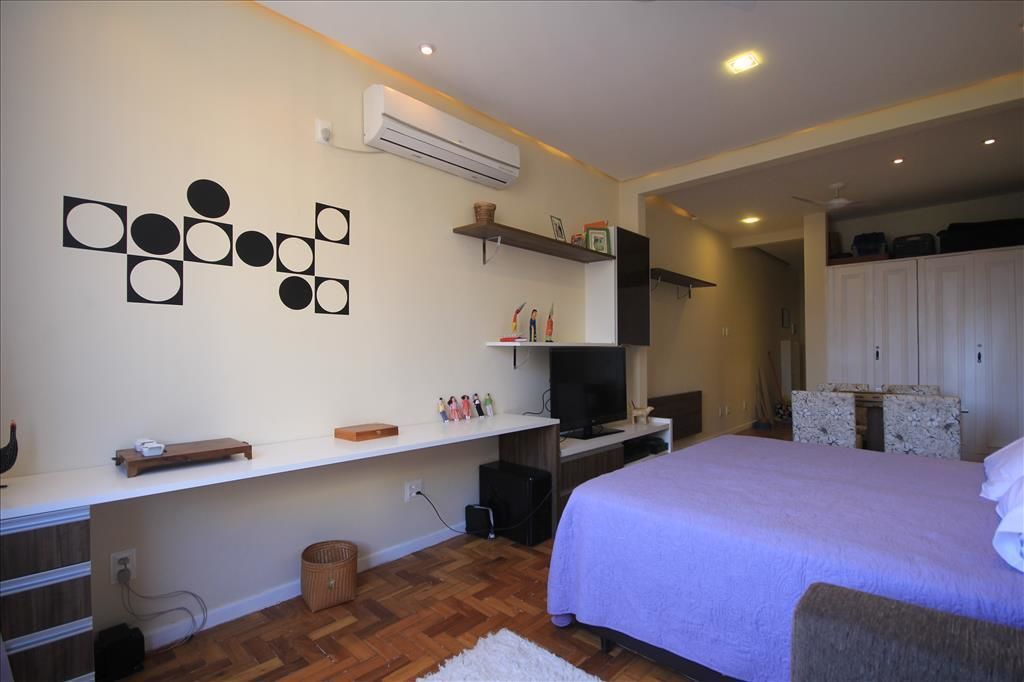 A bedroom with a bed, a TV, a shelf with decorative items, and a wall-mounted air conditioner.