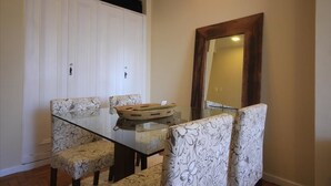 A dining area with a glass table and floral-patterned chairs, a wooden-framed mirror, and a white wardrobe. - Assis 801 (Rio de Janeiro)