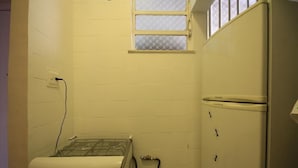 A compact kitchen with a gas stove, a refrigerator, and a small window. - Assis 801 (Rio de Janeiro)