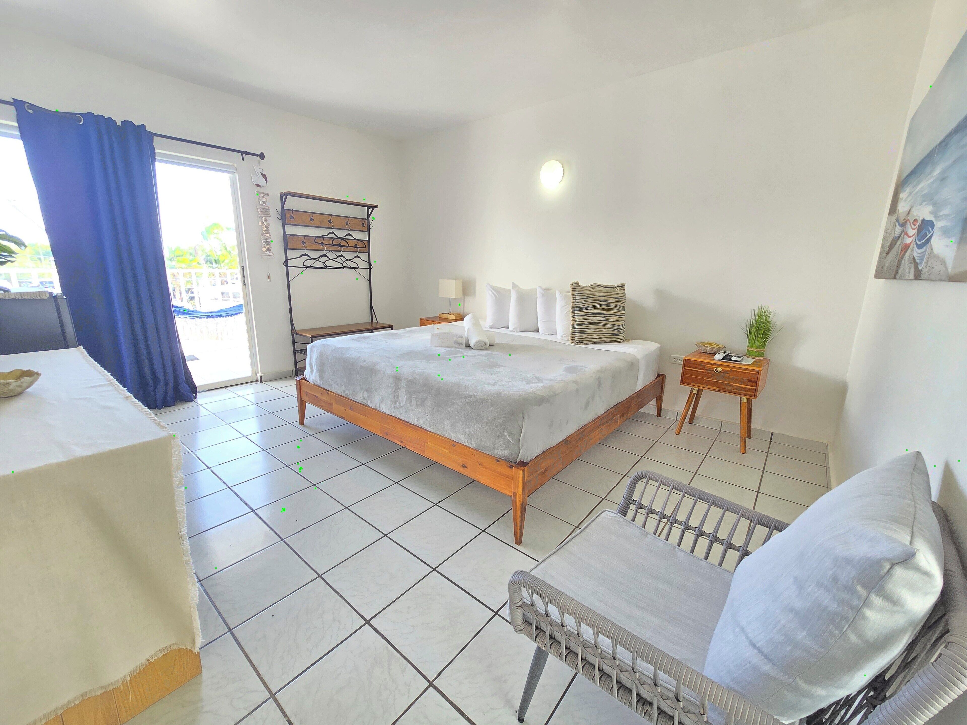 Quarto com cama, cadeira, mesa de cabeceira e janela com cortinas.
