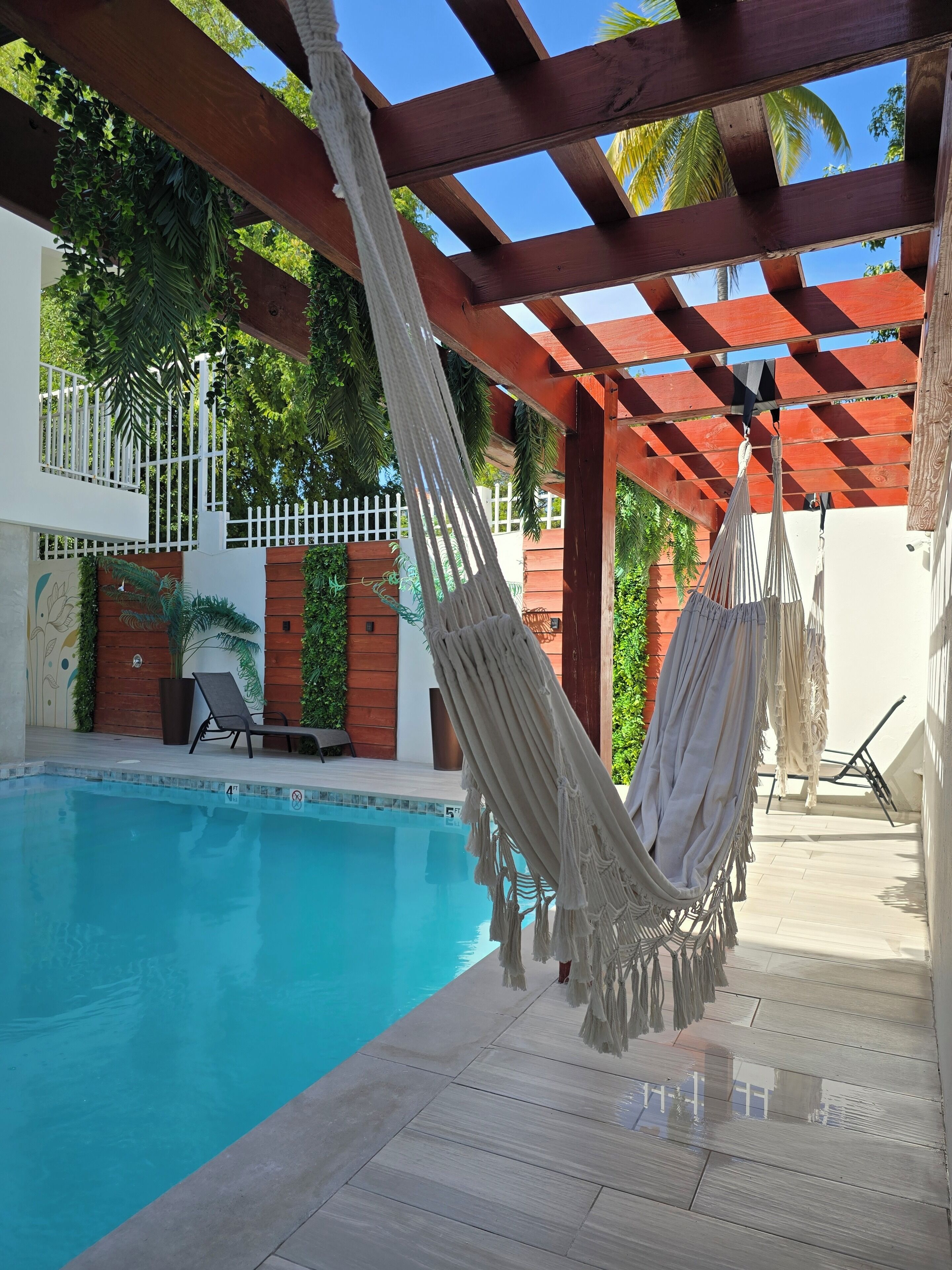 A pool area with a hammock, wooden pergola, and a white fence.